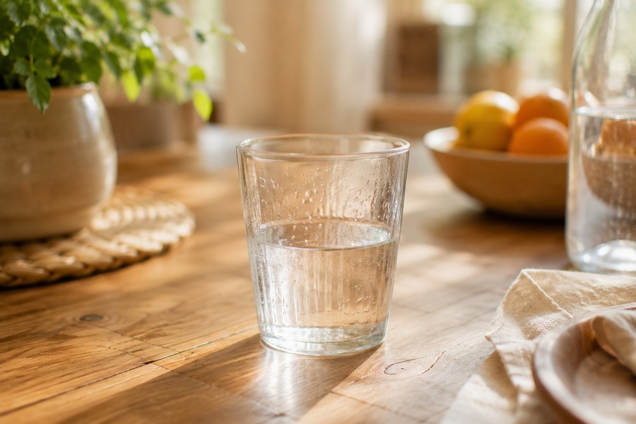 Verre d'eau à moitié rempli sur une table en bois, lumière naturelle